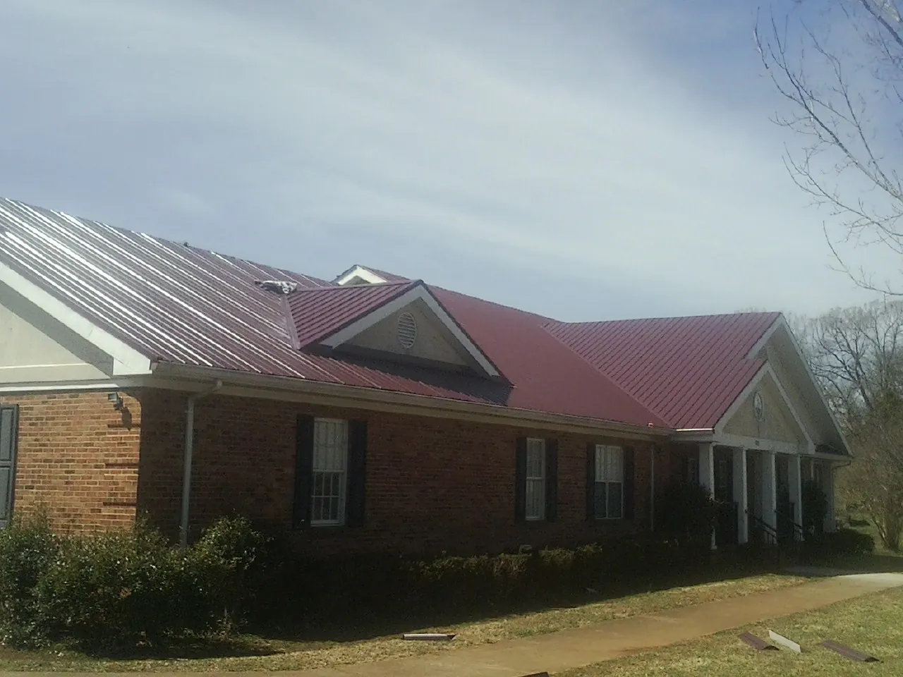 Red metal roof with gabled entries on a long brick building, from a Hail Damage Roof Repair job in Roanoke