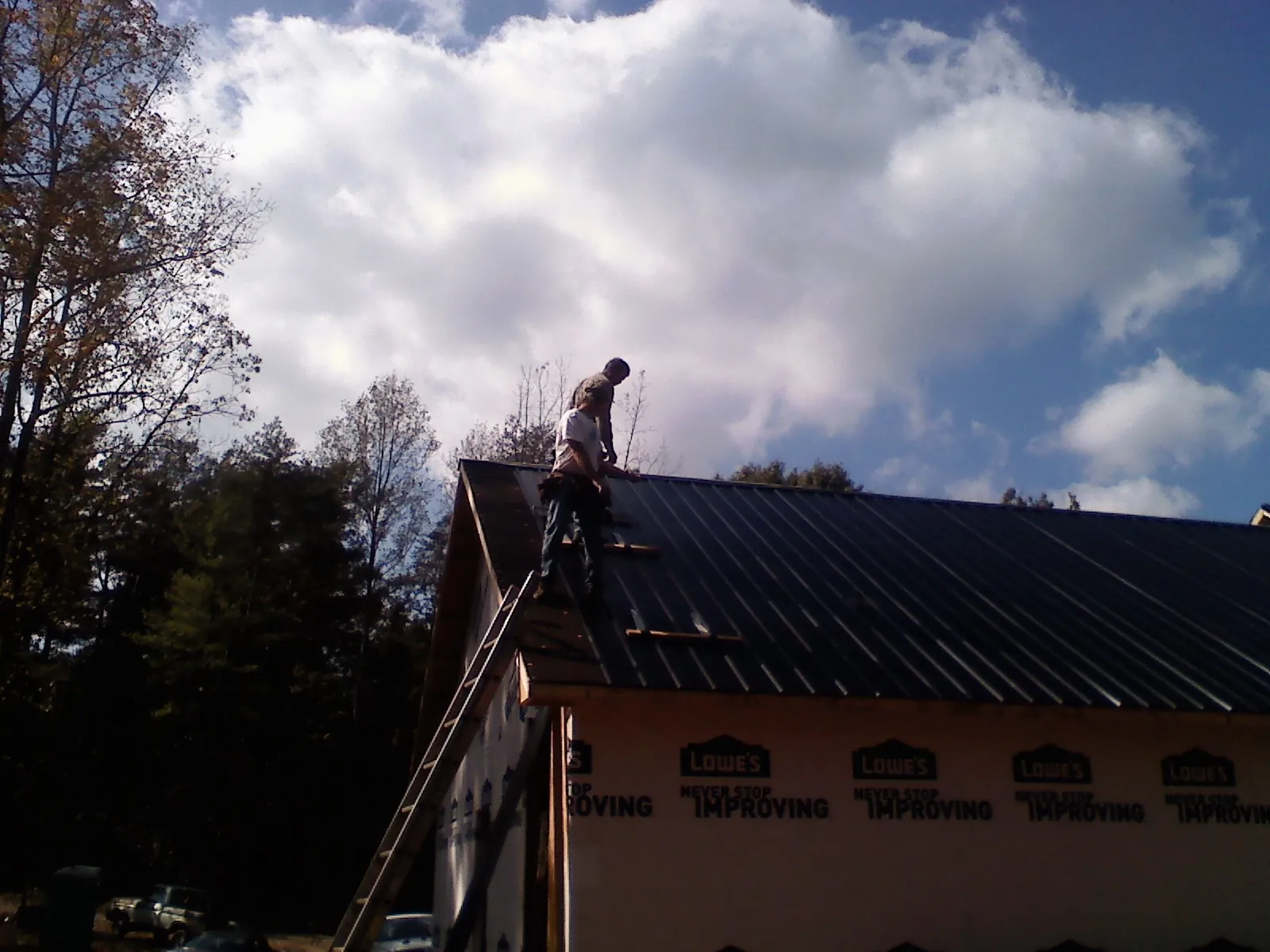Roofer fastening dark metal panels high against a cloudy sky, from a Roof Inspection job in Roanoke